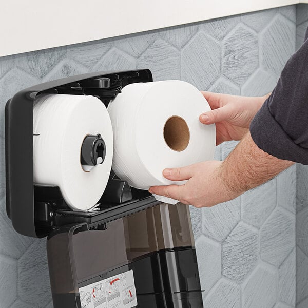 A person holding a Tork Advanced Mini Jumbo Toilet Paper roll.