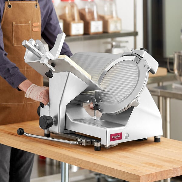 A person in an apron using an Estella manual meat slicer to cut meat.