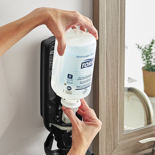 A hand pouring Tork Extra Mild foaming hand soap into a dispenser.