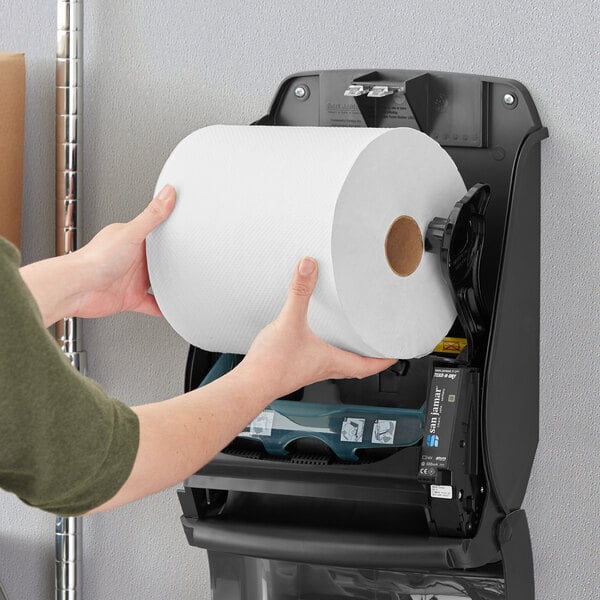 A hand holding a Tork Universal white paper towel roll.