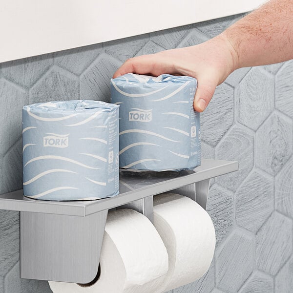 A hand holding a blue box of Tork Advanced toilet paper.