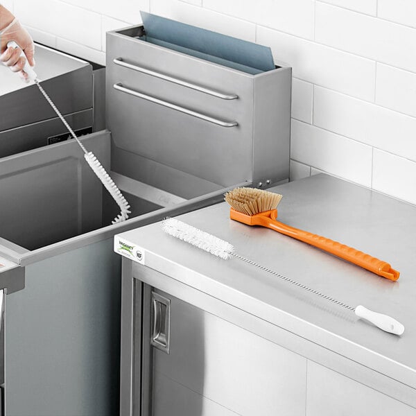 A woman uses a Fryclone deep fryer cleaning brush on a counter.