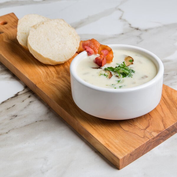 A bowl of Chef's Companion cream soup with bacon and bread on a wooden cutting board.