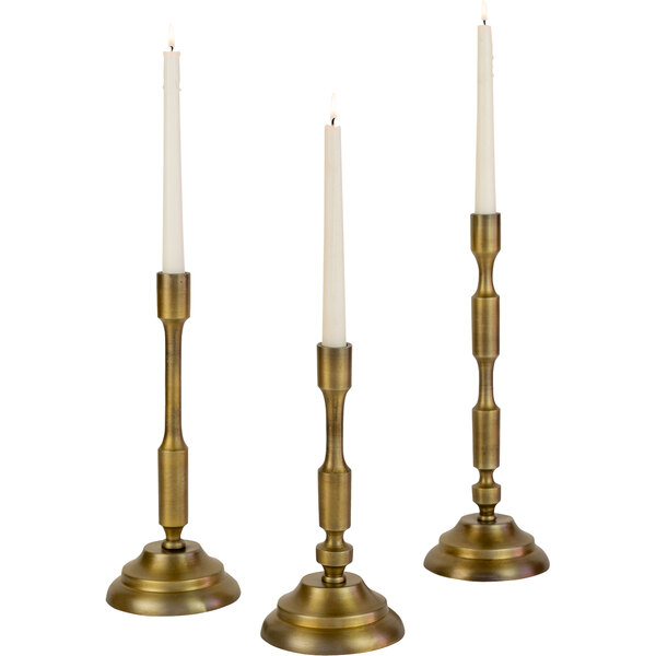 A group of Kalalou antique brass candle holders with lit white candles.