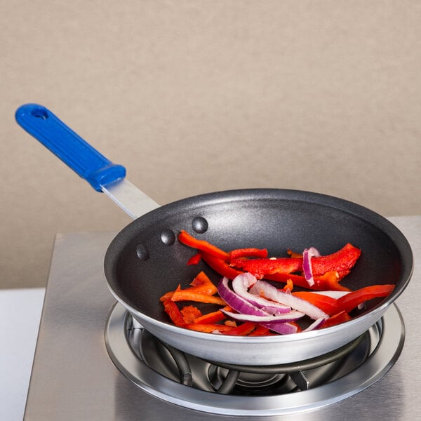 A Vollrath Wear-Ever frying pan with chopped red bell peppers and onions in it.