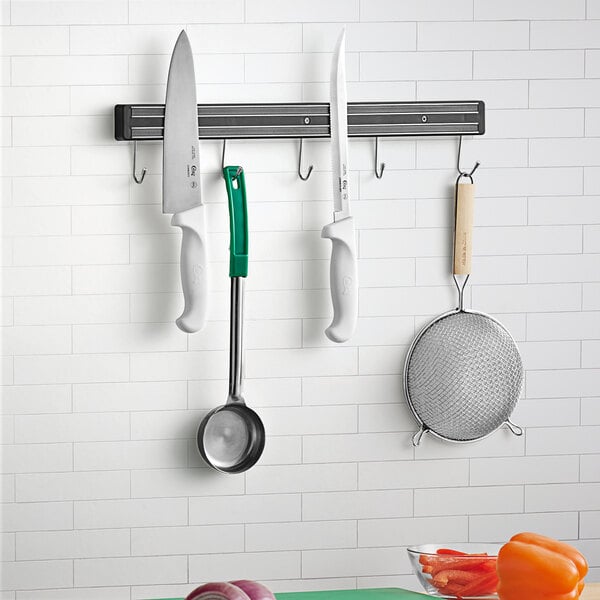 A Choice metal magnetic knife holder with utensils hanging on it.