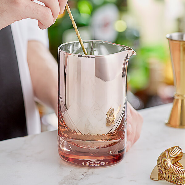 A person stirring a drink in a Barfly rose stirring glass.