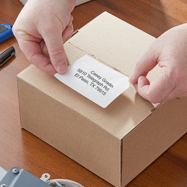 A person putting a Lavex white direct thermal label on a box.