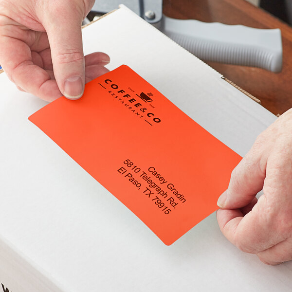 A person's hands using Lavex orange thermal transfer labels to label a box.