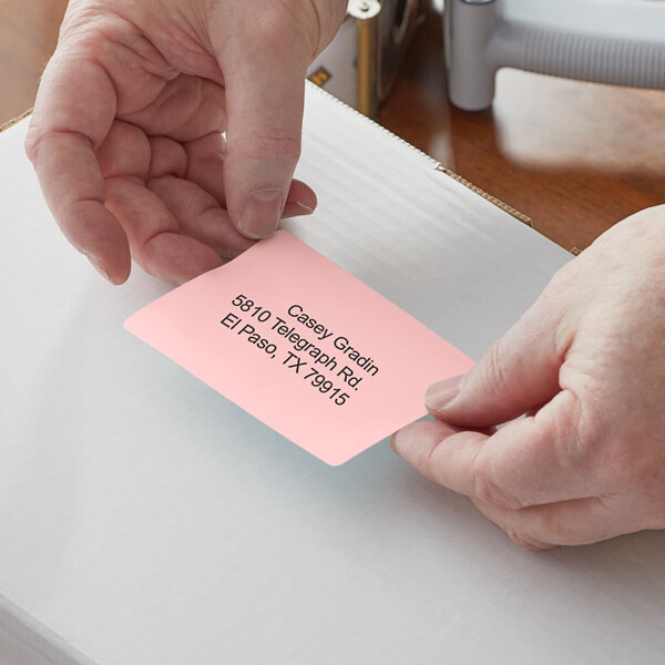 A person's hands using a pink Lavex label on a card.