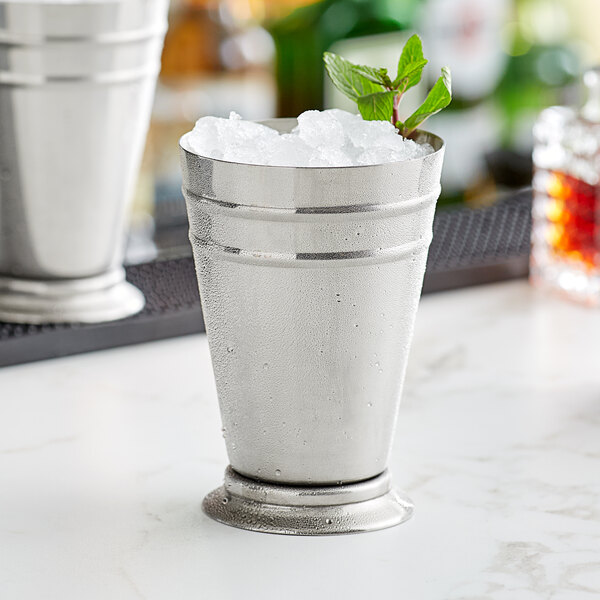 A Barfly stainless steel mint julep cup on a marble surface filled with ice and mint leaves.