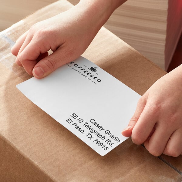 A person's hands holding a stack of white fanfold labels.
