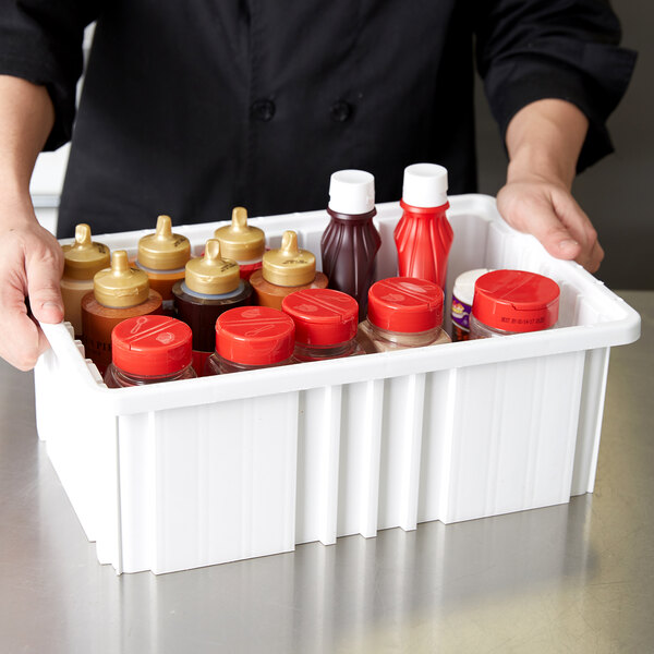 A white Metro tote box with dividers holding red and white condiment bottles.