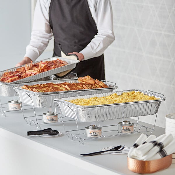 A man in an apron using Choice disposable chafer dishes on a hotel buffet table.