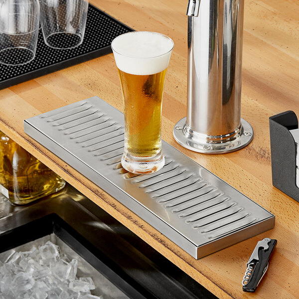 A Regency stainless steel surface mount beer drip tray under a glass of beer on a bar counter.