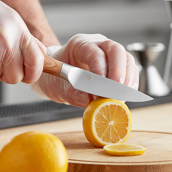 A person slicing a lemon with an American Metalcraft stainless steel paring knife.