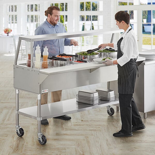 A man and woman standing in front of a ServIt stainless steel ice-cooled food table.