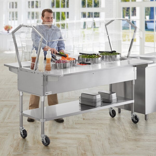 A man standing behind a ServIt stainless steel ice-cooled food table with sneeze guard and side trays.