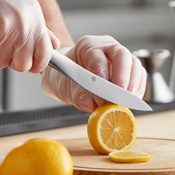 A person in gloves using an American Metalcraft stainless steel paring knife to slice a lemon.