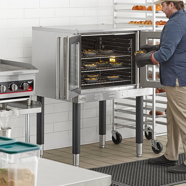 A man standing next to a Main Street Equipment convection oven with bread on a tray.