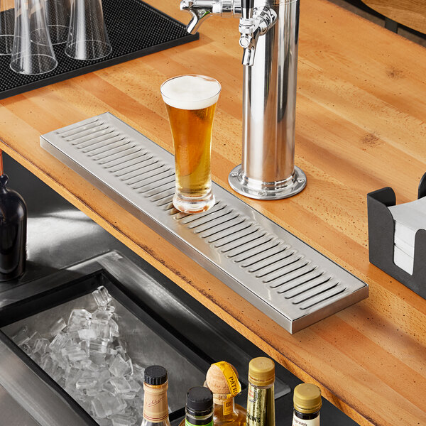 A Regency stainless steel beer drip tray on a bar counter with a glass of beer.
