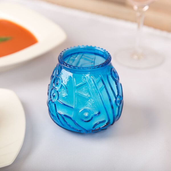 A blue glass vase with a blue Venetian candle on a table.