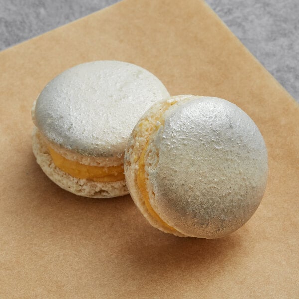 Two yellow and white Macaron Centrale honey butterscotch macarons on a table with brown paper.