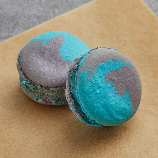 Two blue and grey Macaron Centrale cookies and cream macarons on a brown surface.