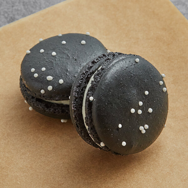 Two black Macaron Centrale cookies with white sprinkles on top.