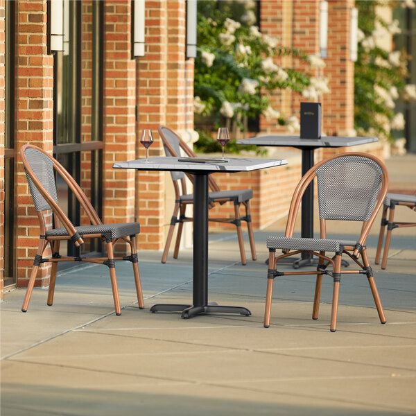 A Lancaster Table & Seating Versilla table with 2 French Bistro chairs on a patio.