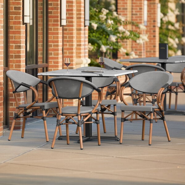 A Lancaster Table and Seating square table with black and white chairs on an outdoor patio.