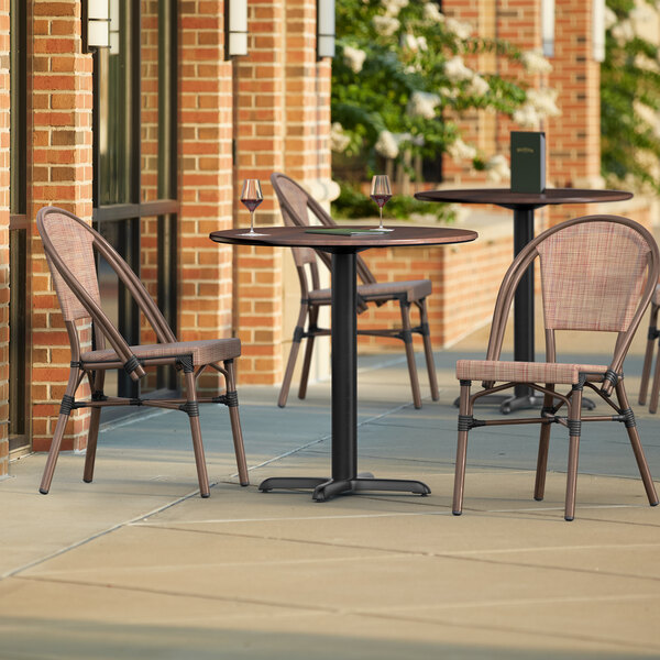 A Lancaster Table & Seating Excalibur round walnut table with two chairs on an outdoor patio.