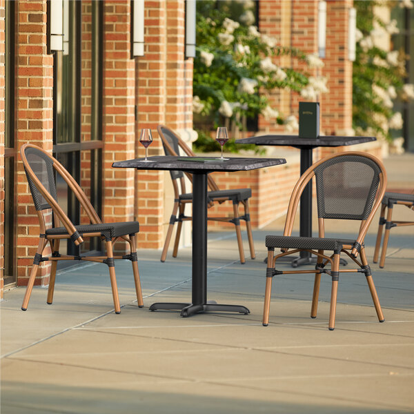 A Lancaster Table & Seating Paladina table with black chairs on an outdoor patio.