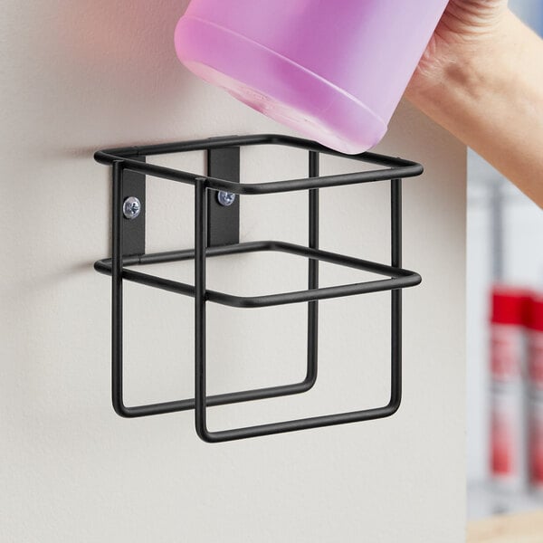 A person pouring a pink bottle into a black Lavex wall-mount holder.