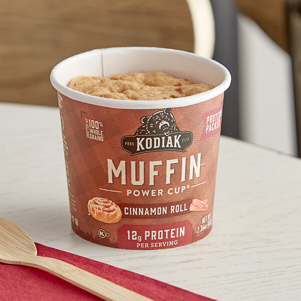 A Kodiak Cakes cinnamon roll minute muffin cup on a table with a wooden fork