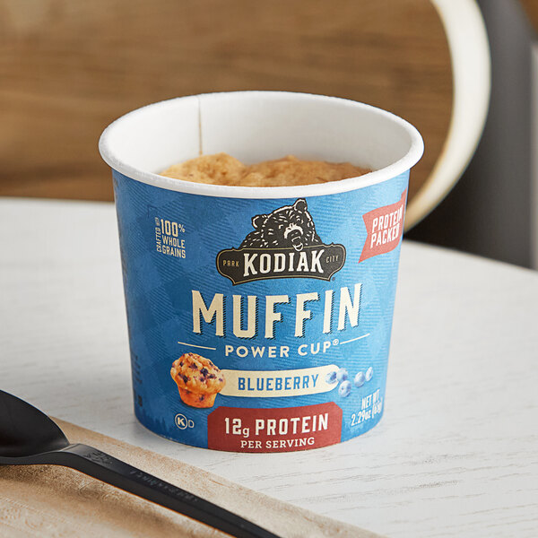 A blue and white container of Kodiak Cakes Blueberry Minute Muffin on a table.