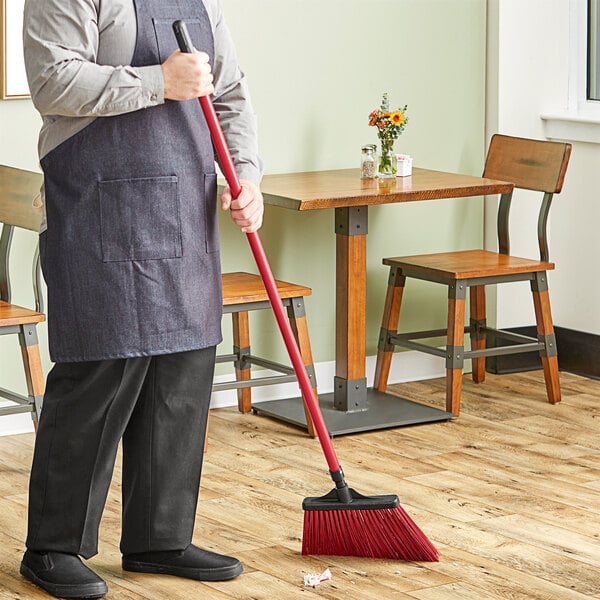 A man using a Lavex red angled broom with a metal handle to sweep the floor.