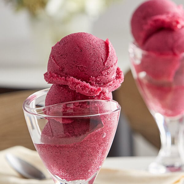 A glass cup filled with pink Pitaya Dragon Fruit Sorbet with red berries on top.