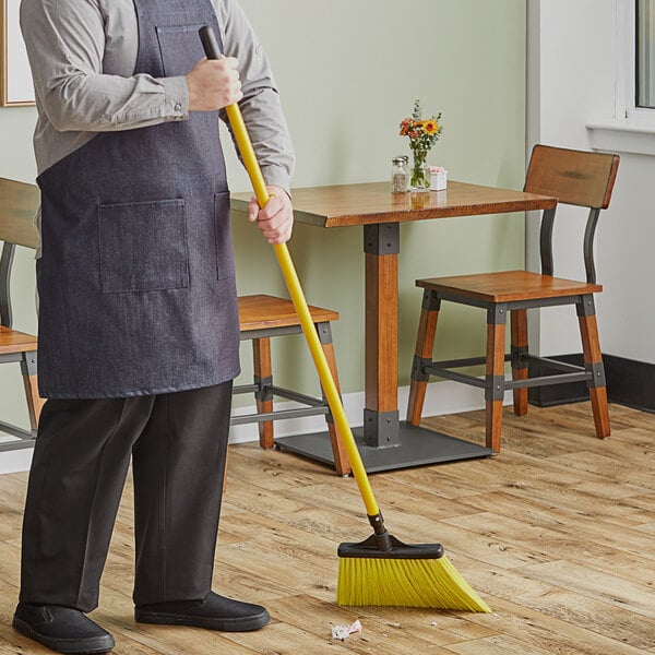 A person using a Lavex yellow broom with a yellow handle to sweep the floor.