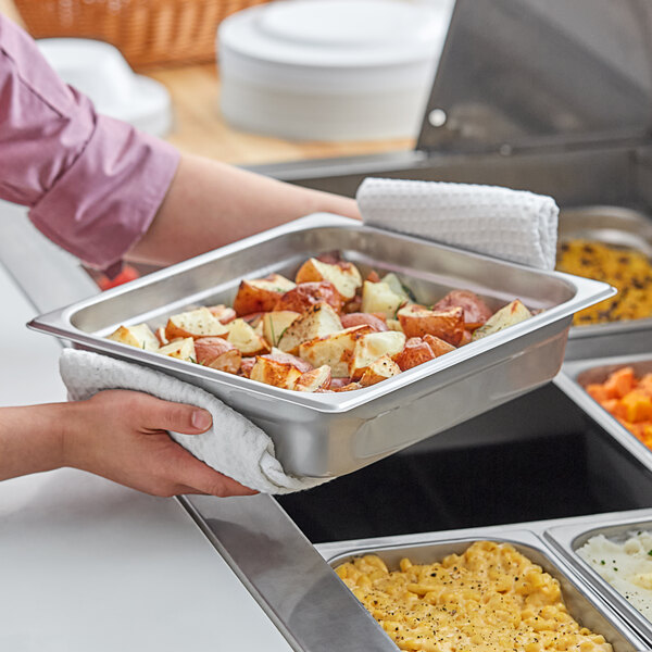 A person holding a tray of food in a Choice Classic half size chafer pan.