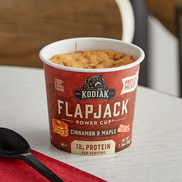 A Kodiak Cakes Cinnamon and Maple Flapjack Cup on a table with a black spoon.