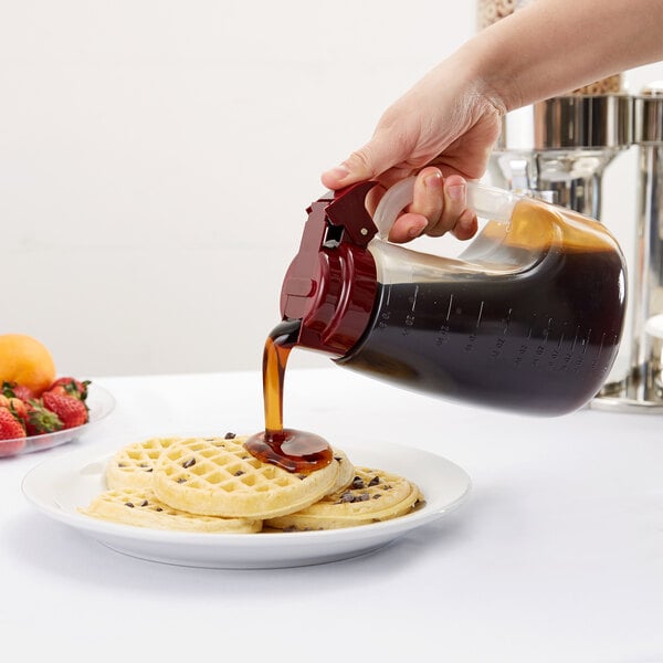 A hand pouring syrup from a Tablecraft dispenser onto a plate of waffles.