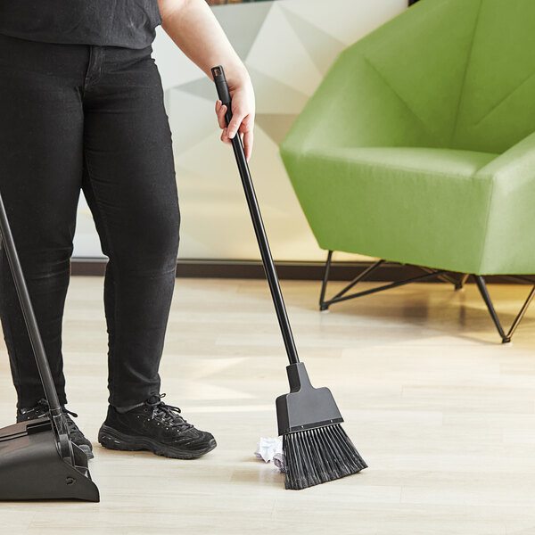 A woman using a Lavex lobby broom to sweep the floor.