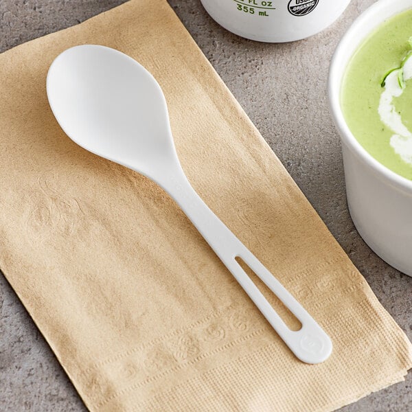 A white World Centric compostable soup spoon on a napkin next to a cup of soup.