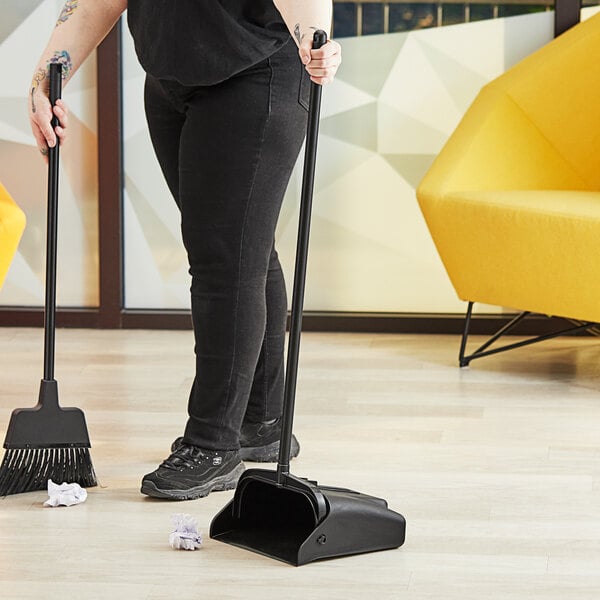 A woman using a Lavex broom and dustpan to clean up.