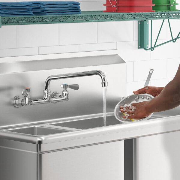 A person washing dishes in a sink using a Regency wall mount faucet.