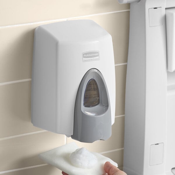 A hand using a Rubbermaid white foam soap dispenser.