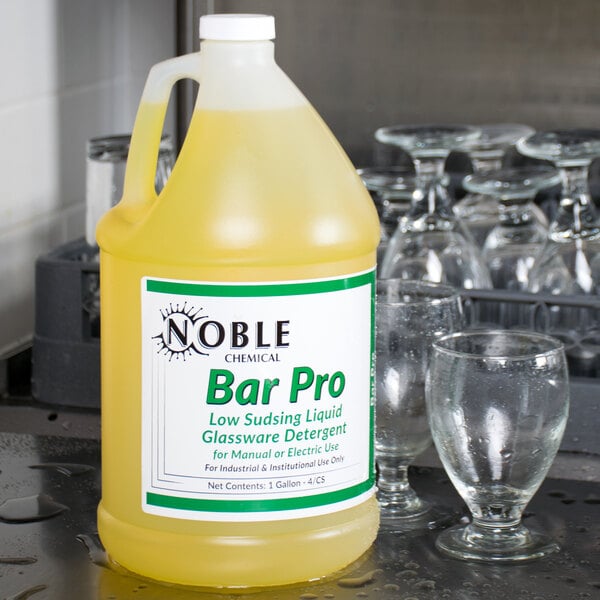 A white bottle of Noble Chemical Bar Pro liquid detergent on a bar counter next to glasses.