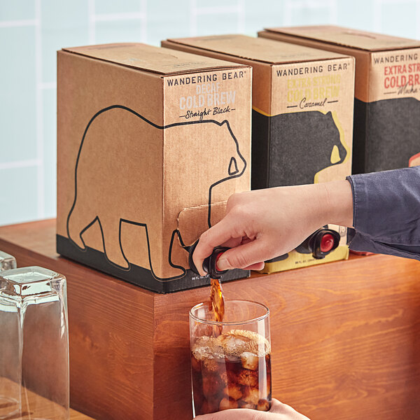 A person pouring Wandering Bear decaf cold brew coffee into a glass with ice.