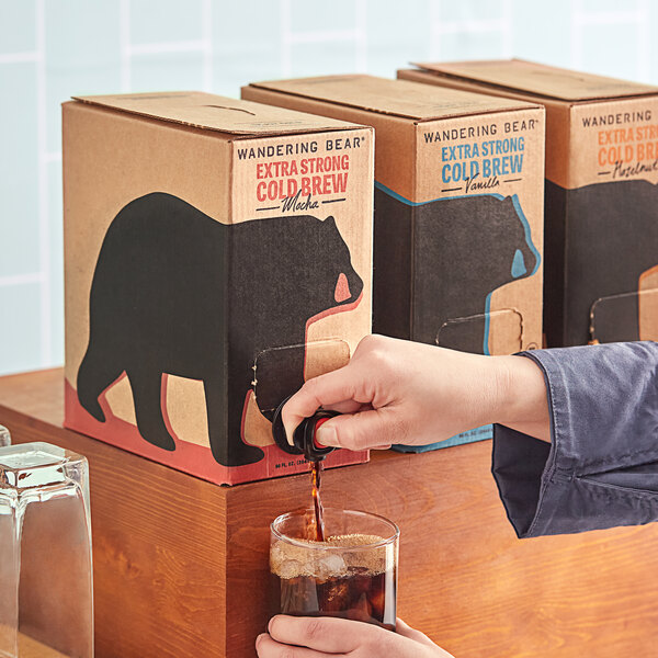A hand pouring Wandering Bear Organic Mocha Cold Brew Coffee into a brown box with a black handle.